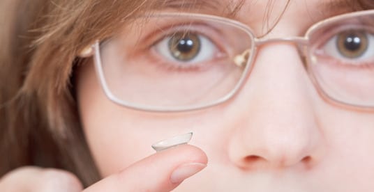 Woman in glasses contemplating contact lenses
