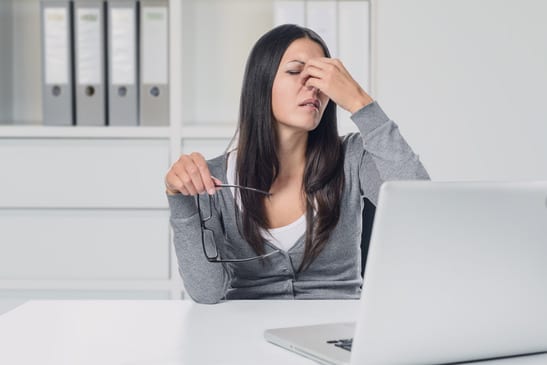 Young woman suffering from eye strain at her laptop removing her eyeglasses to rub her eyes with her finger with a pained expression