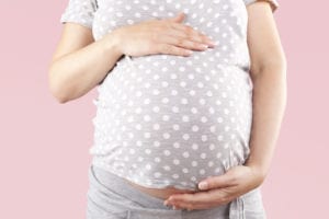 Pregnant beautiful woman touching big belly isolated on pink background. Pregnancy and motherhood.